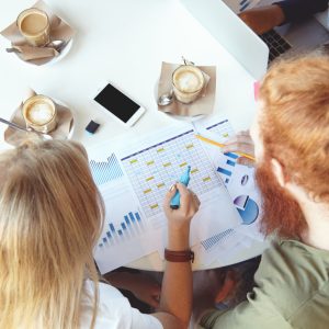 Top view of young ambitious and creative people brainstorming, discussing plans and making notes on paper, developing business strategy for startup project while sitting at table at coffee shop